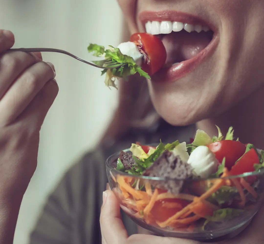 Woman taking a bit of vegetable salad from fork