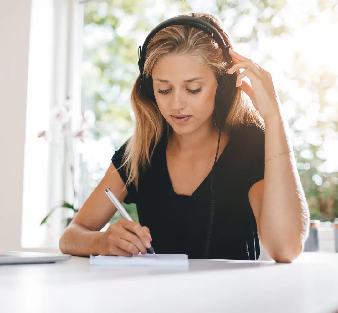 Woman listeng to headphones and writing on a notepad